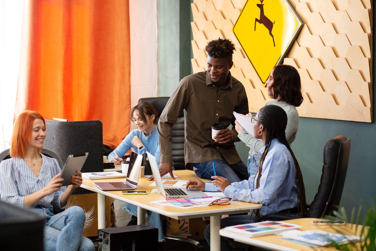 Four professionally dressed African professionals—two men and two women—smiling and gathered around a laptop, engaged in a collaborative discussion.